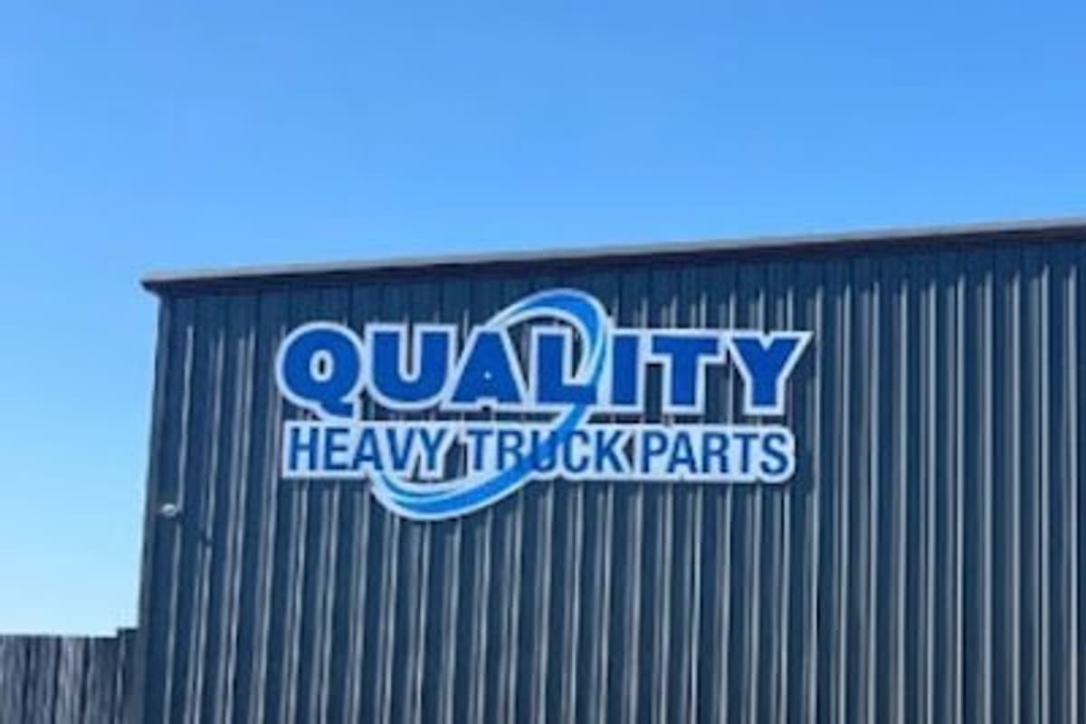 Valley Heavy Equipment & Used Parts: Large blue sign reading Quality Heavy Truck Parts on the side of a gray metal building under a clear blue sky