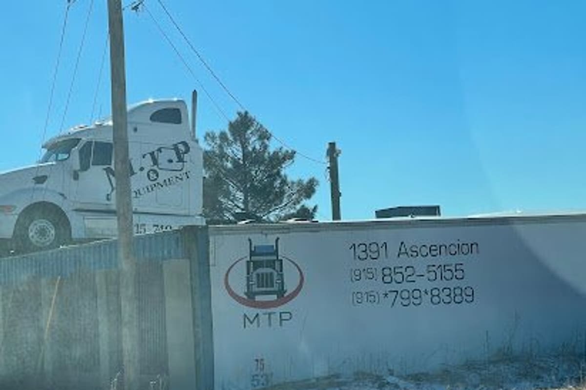 M. T. P. & Equipment: White trailer wall painted with a truck logo, address and phone numbers, with a white semi truck cab behind a fence