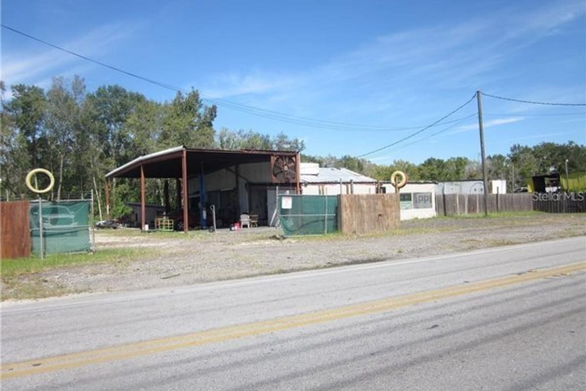Lakeland Salvage Yard: Open-sided metal shop building and fenced gravel lot beside a rural road under a blue sky