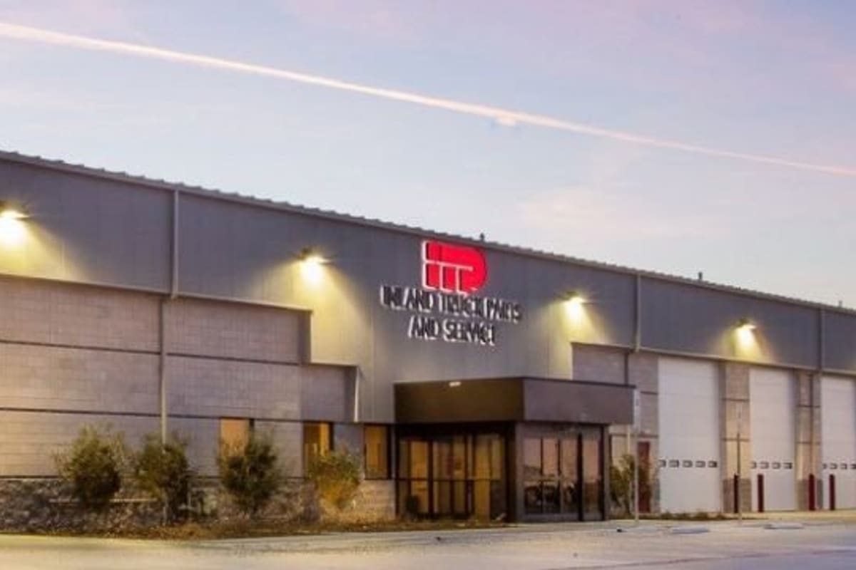 Inland Truck Parts & Service: Long gray truck service building with multiple white bay doors and glass entrance at dusk