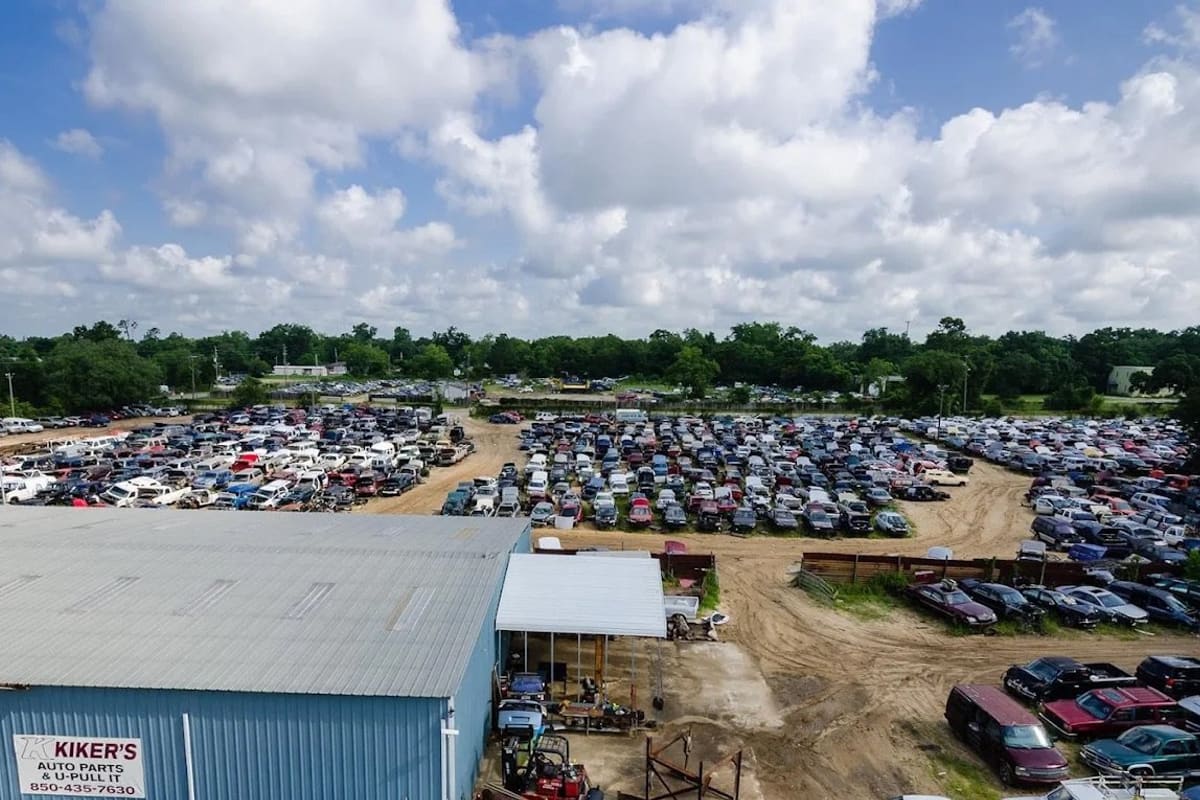 Kikers U-Pull-It: Aerial view of a large salvage yard with rows of cars beside a blue metal shop building with a sign