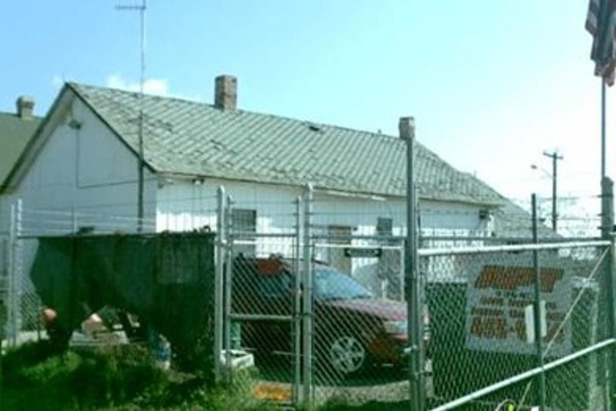 Big Daddy's Towing.com: White single-story building with a worn metal roof behind a chain-link fence and gate, with a car parked inside