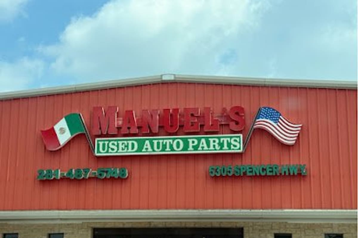 Manuel's Used Auto Parts: Red metal building with a large sign reading Used Auto Parts, flanked by Mexican and American flags, under a cloudy sky