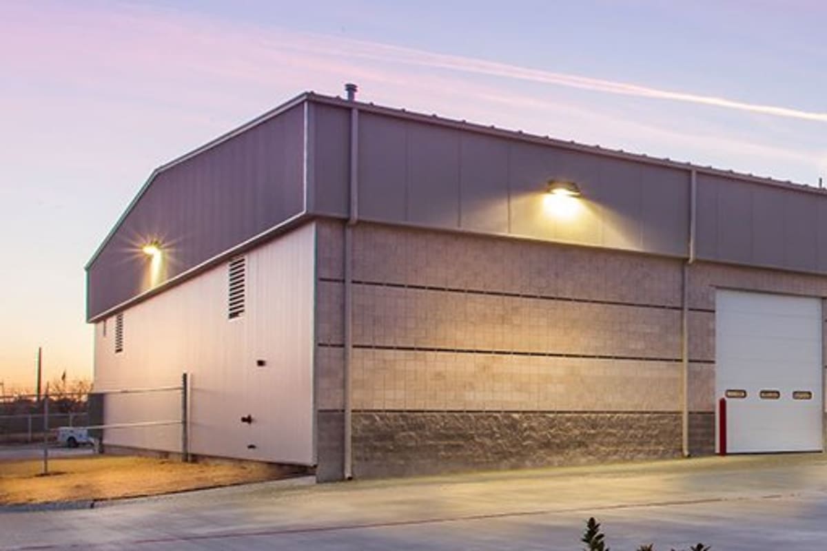 Inland Truck Parts & Service: Large gray industrial building with garage bay doors and a lit red logo sign at dusk
