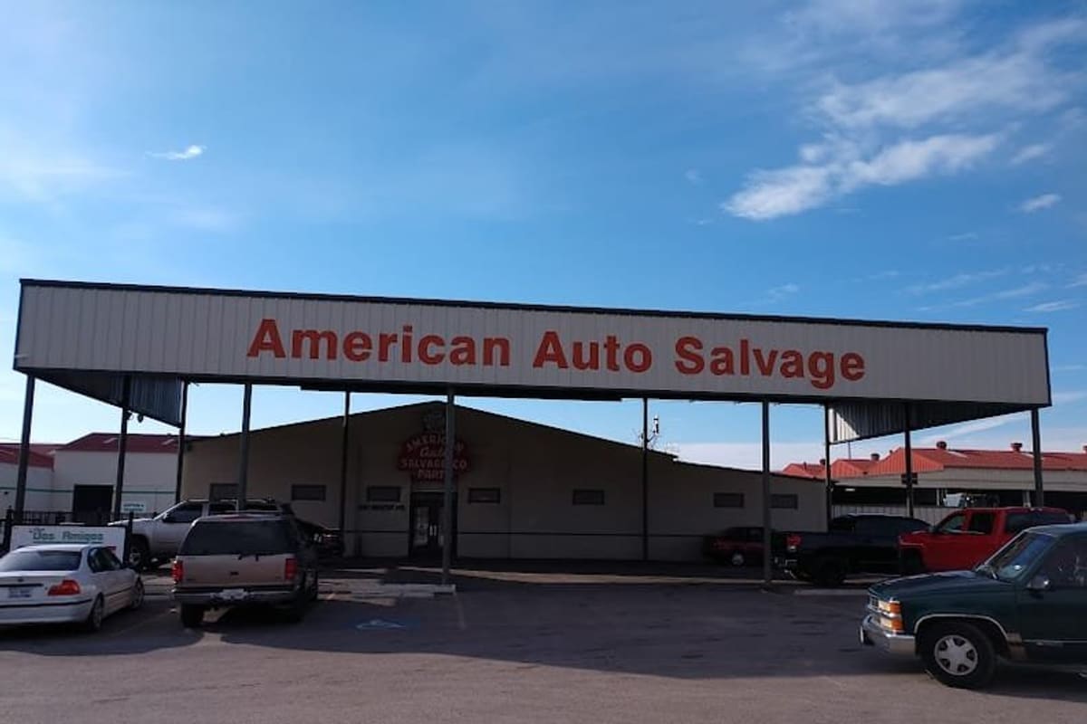 American Auto Salvage: Wide daytime view of a salvage yard building with a large covered canopy sign above a parking lot with several vehicles