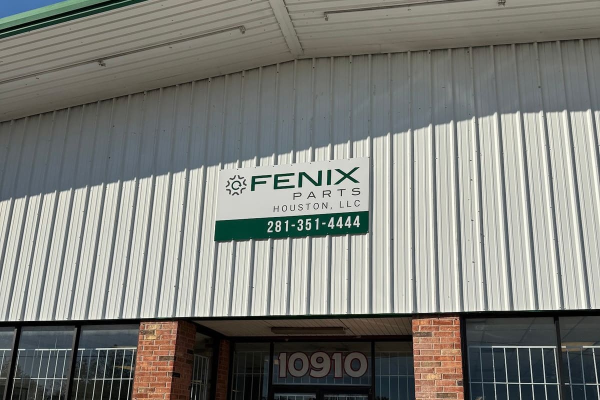 Fenix Parts - Houston: Brick and metal-sided building with a green-trimmed roof, a sign above the barred glass entrance, and number 10910