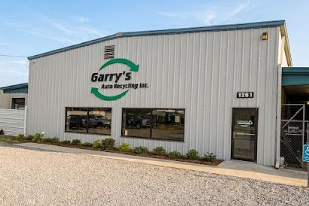 Garry's Auto Recycling: Metal office building with green recycling logo sign, glass entrance door, landscaped beds and a gravel parking area