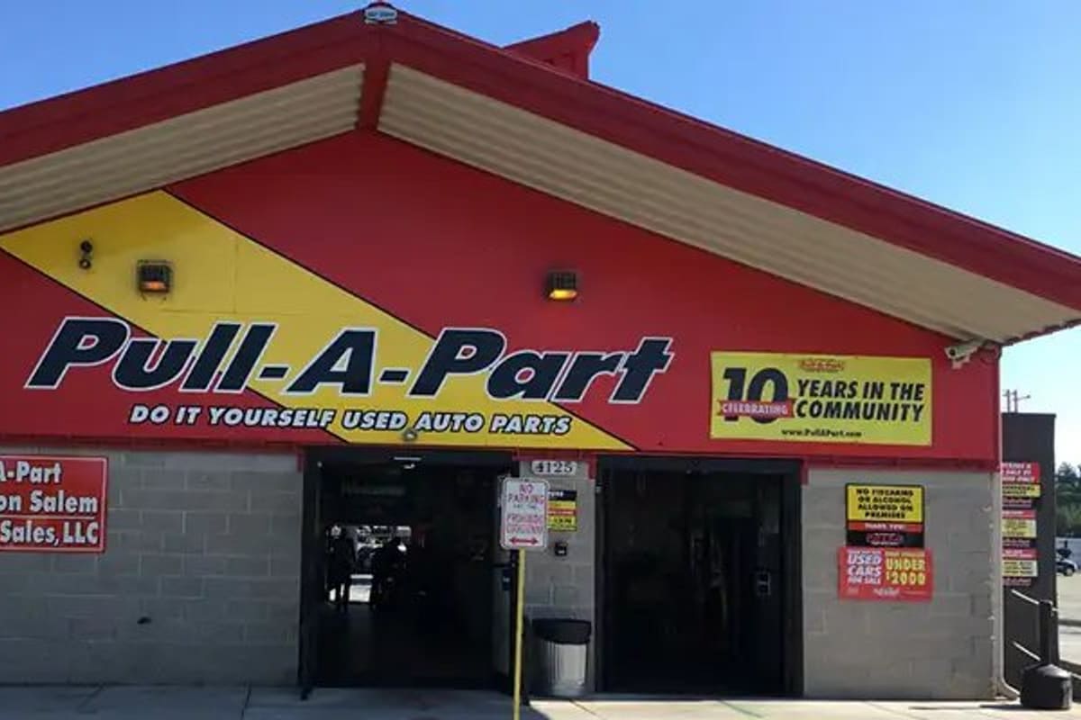 Pull-A-Part Winston-Salem: Red and yellow self-service auto parts building with open entrance doors and signs on a cinder block wall
