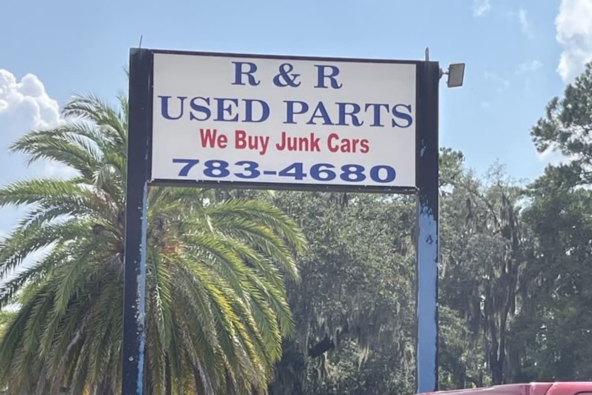 R & R Used Parts: Tall roadside sign reading R & R Used Parts, We Buy Junk Cars, with a phone number, beside a palm tree and a red pickup