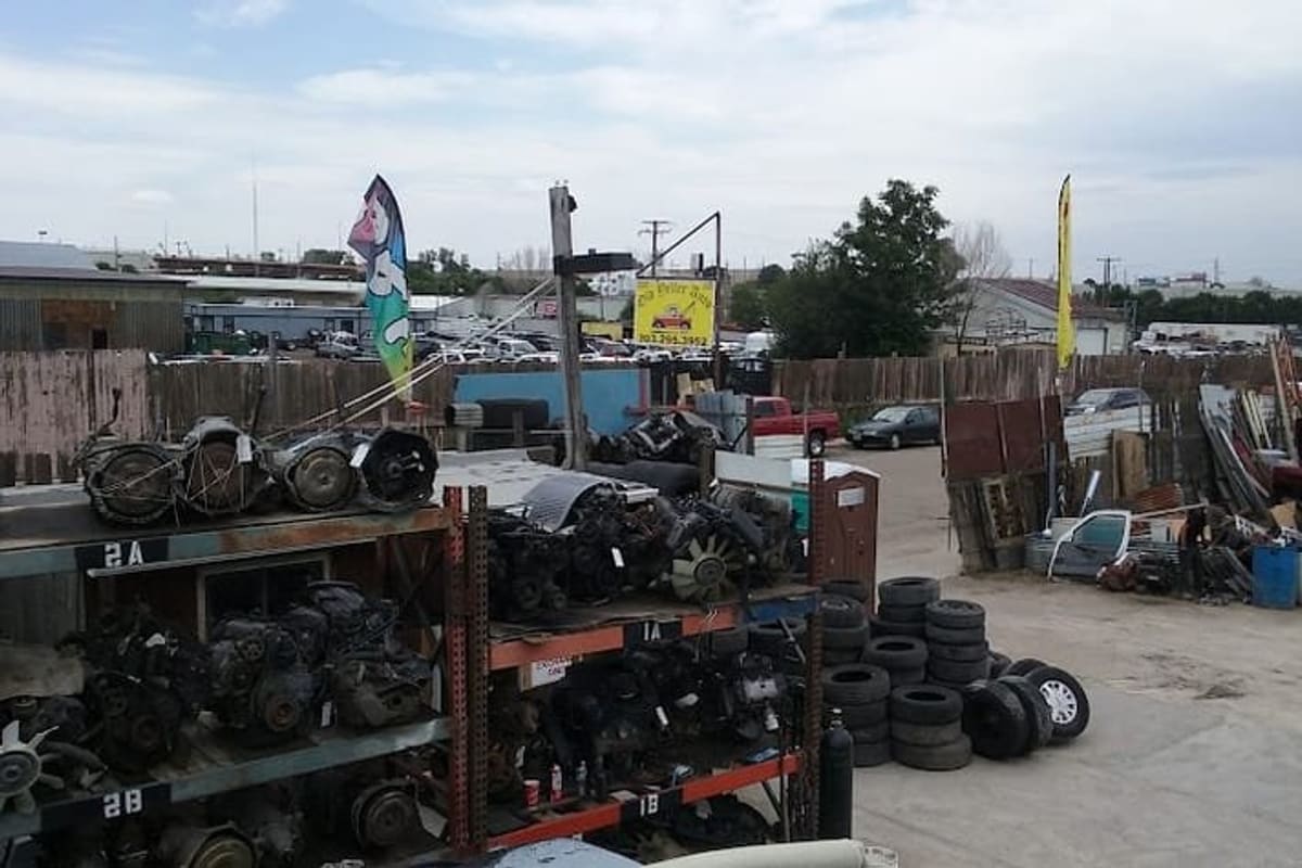 Old Yeller Auto: Open salvage yard with shelves of used engines, stacks of tires and parked vehicles under a partly cloudy sky