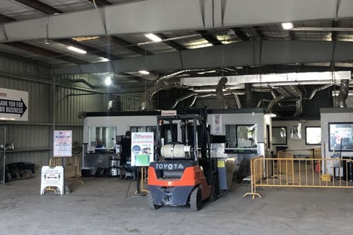 Pick Your Part - West Palm Beach: Covered work area with cashier booths, a forklift and yellow barricades inside a large metal-roofed warehouse