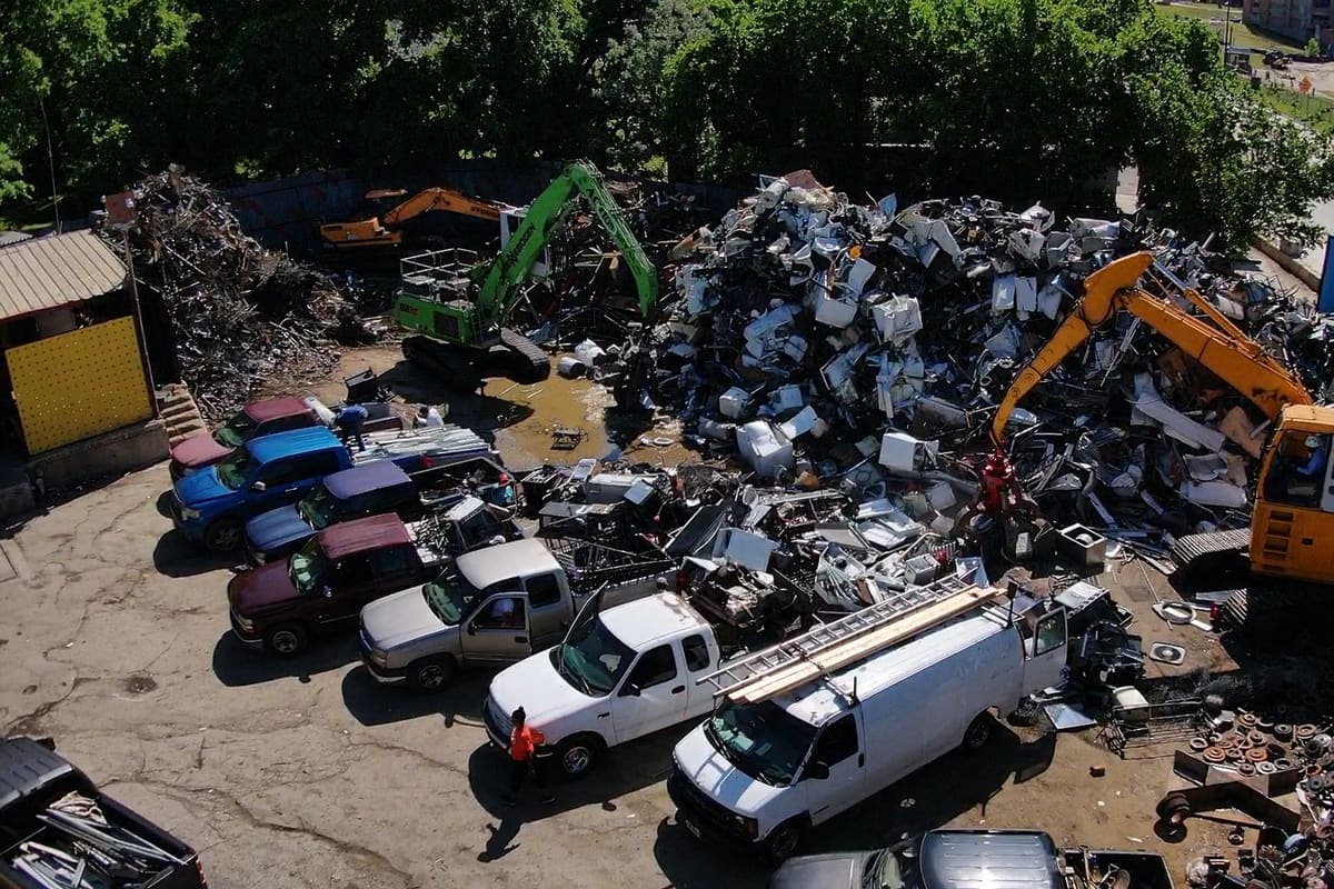 Action Metals Recyclers: Aerial view of a scrap metal yard with excavators, piles of scrap, and pickup trucks lined up to unload