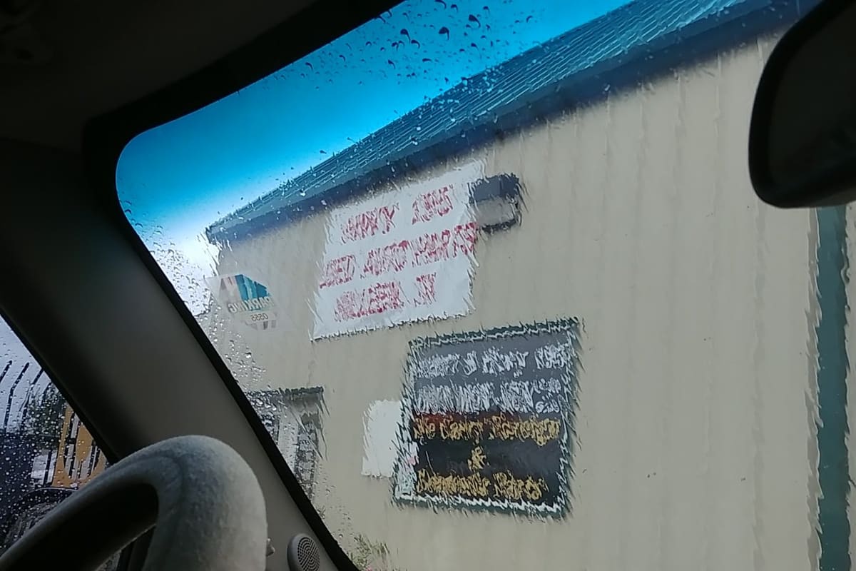Hwy 195 Used Auto Parts: Tan metal building with a hand-painted sign and a chalkboard sign, seen through a rainy car windshield