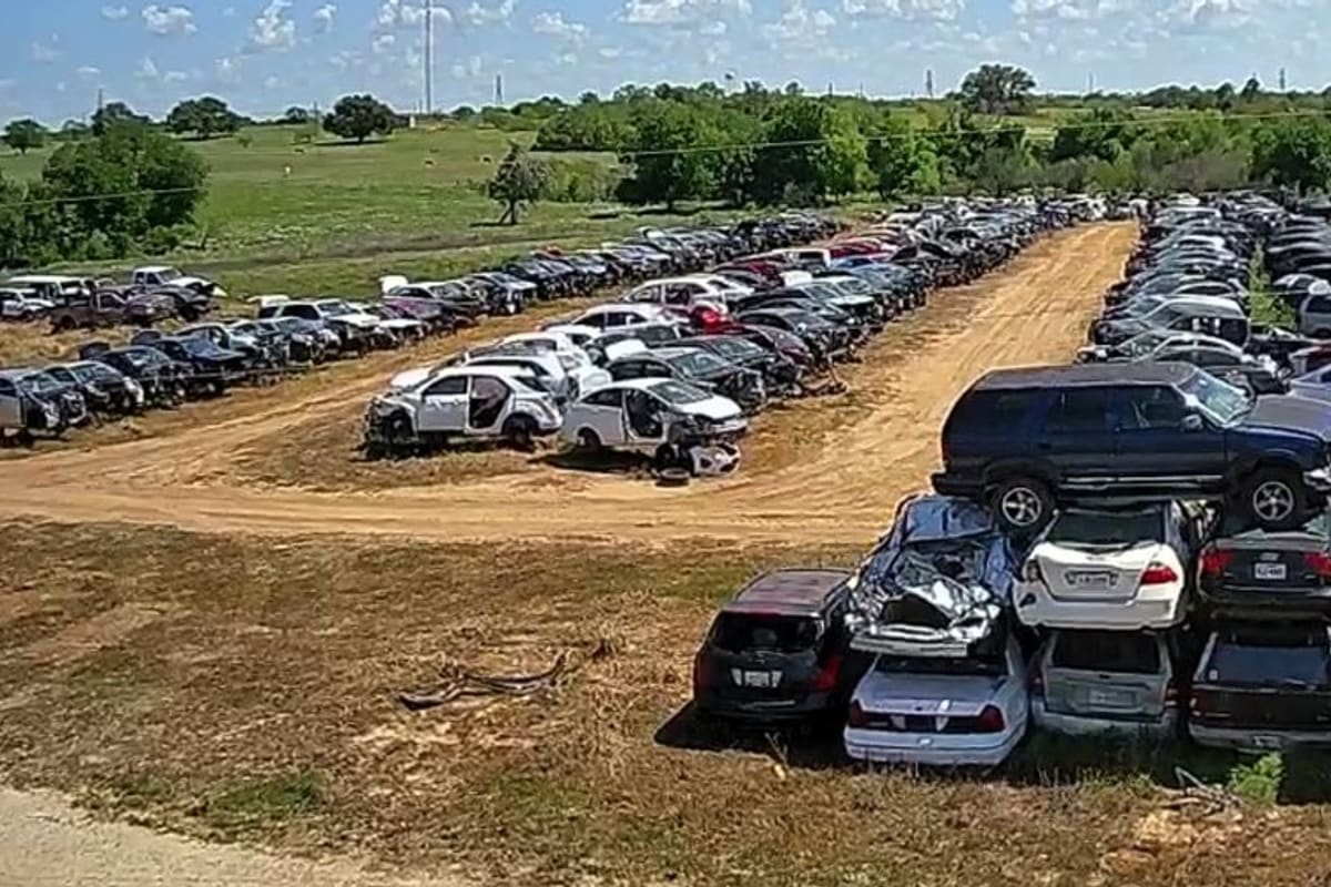 Top Gun Auto Parts: Aerial view of a salvage yard with rows of wrecked cars parked along dirt lanes and stacked vehicles in the foreground