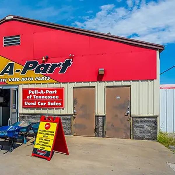 Pull-A-Part Nashville: Red and yellow single-story building with open glass entrance doors, wheelbarrows and an A-frame sign on the concrete lot