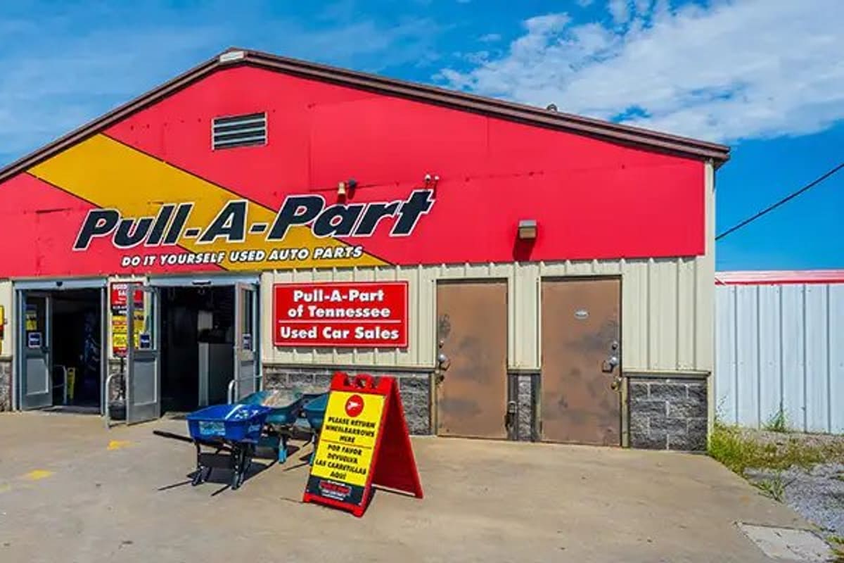 Pull-A-Part Nashville: Red and yellow single-story building with open glass entrance doors, wheelbarrows and an A-frame sign on the concrete lot