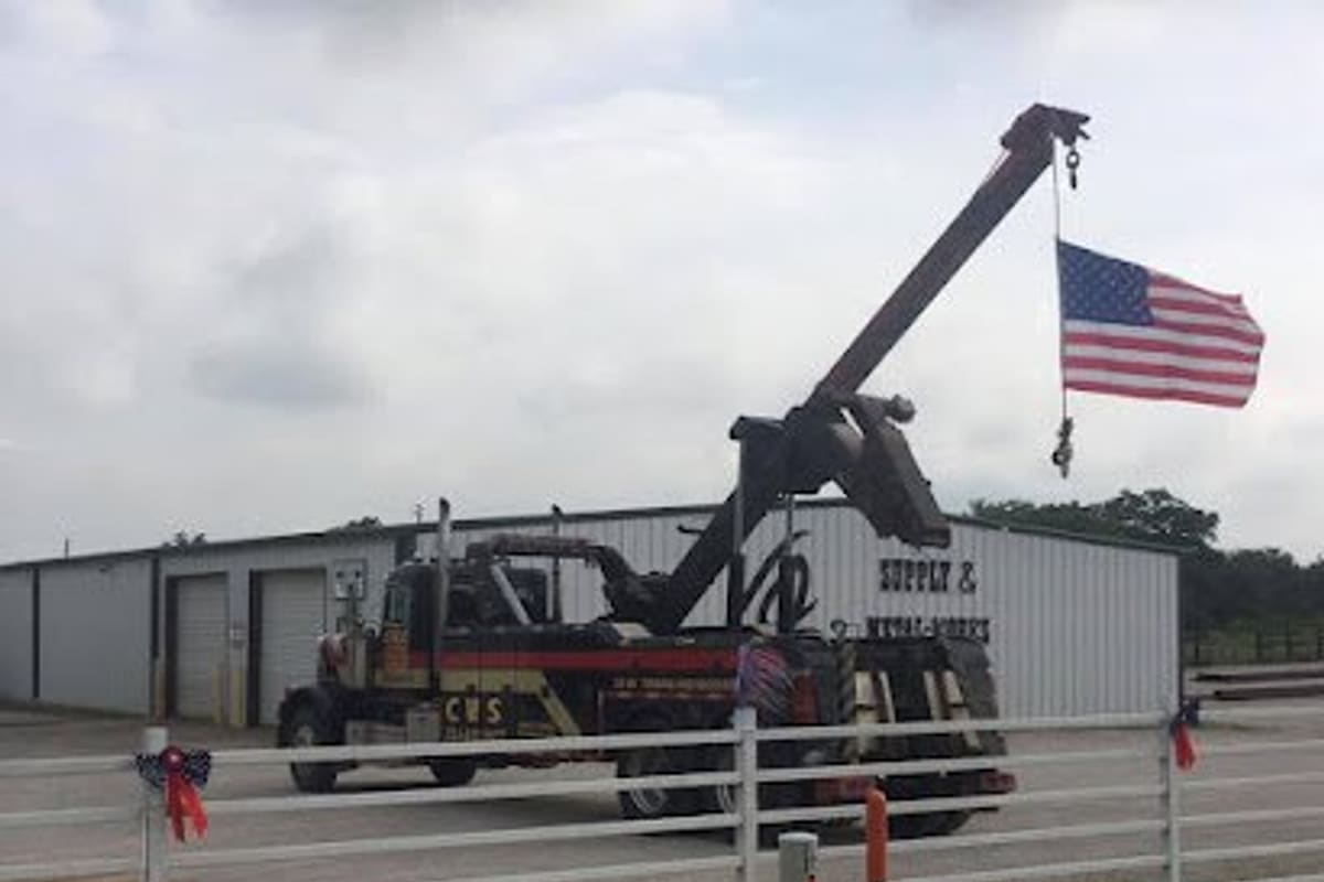 Cisco Wrecker Service Towing & Recovery: Metal shop building behind a white fence with a large wrecker truck parked in front and an American flag hanging from its boom