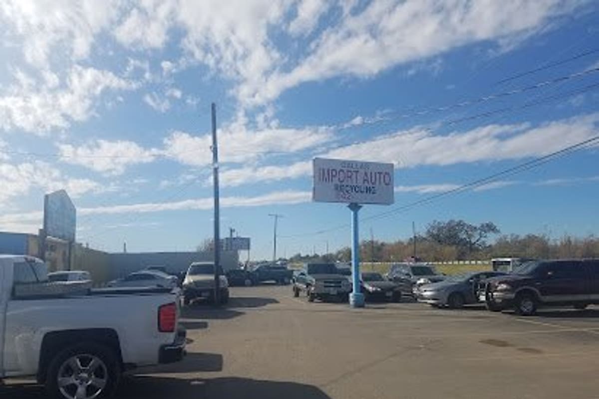 U Pull It Auto & Truck Salvage: Gravel lot with parked trucks and cars beneath a tall pole sign on a sunny day with blue sky and clouds