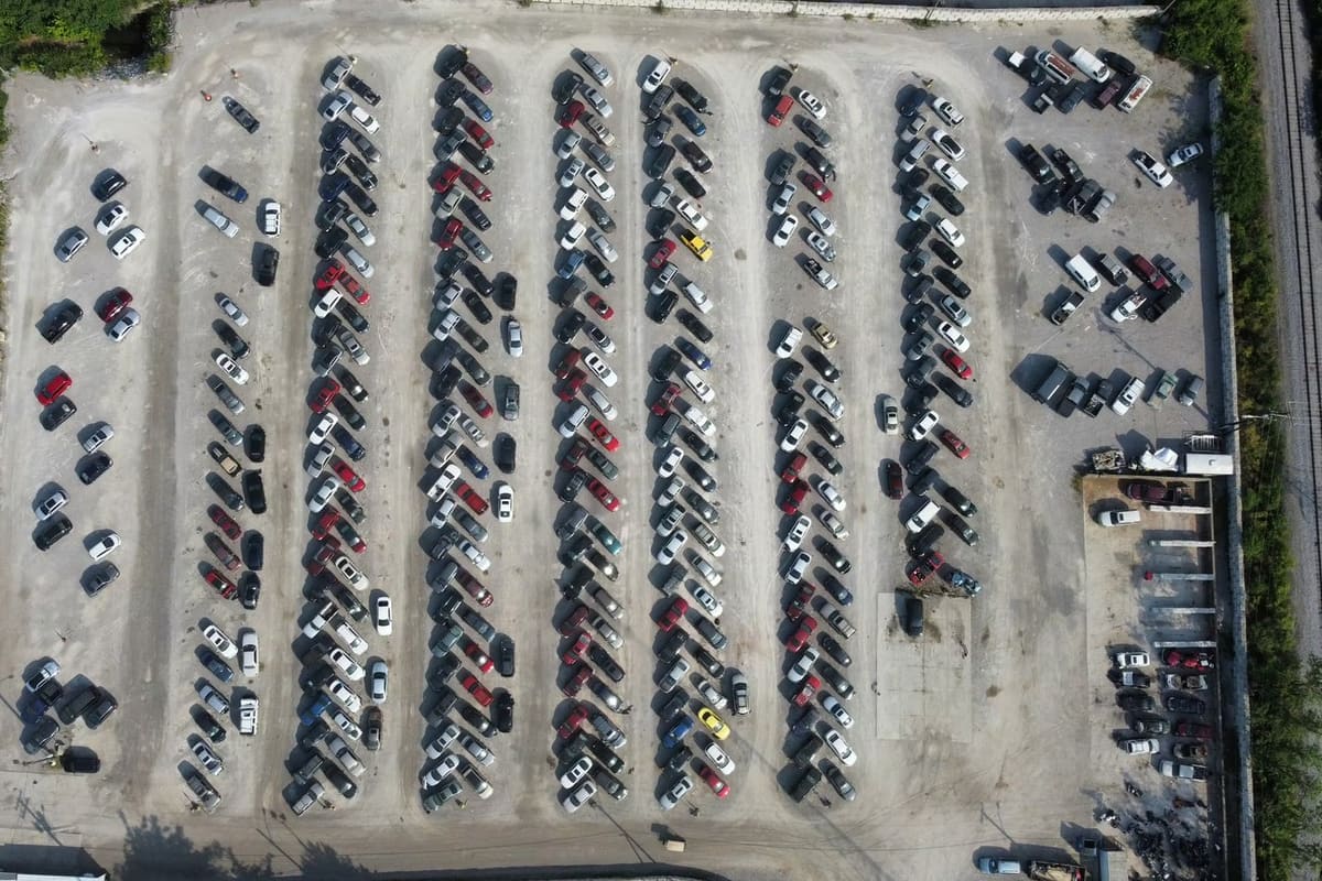 American and Import Auto Parts: Aerial view of a salvage yard with long rows of parked cars on a gravel lot beside a railroad track