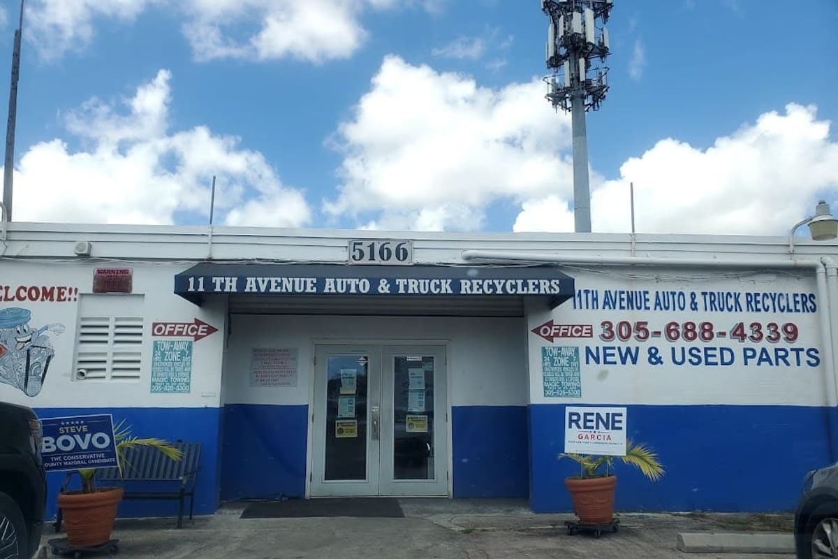 11th Avenue Auto Recyclers: Front of a white and blue single-story office building with double glass doors, an awning, painted signs and potted palms