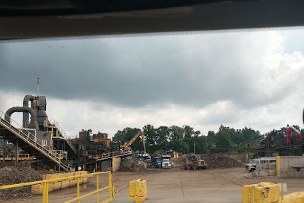 Omnisource: View from a vehicle of a scrap yard with processing equipment, a crane and piles of metal under a cloudy sky