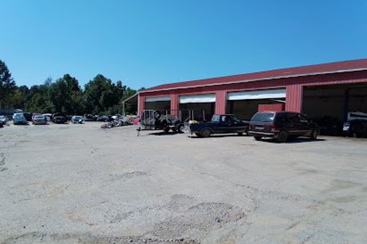 Tennessee Auto Salvage: Wide view of a gravel lot with parked vehicles in the distance and a red metal shop building with open bays