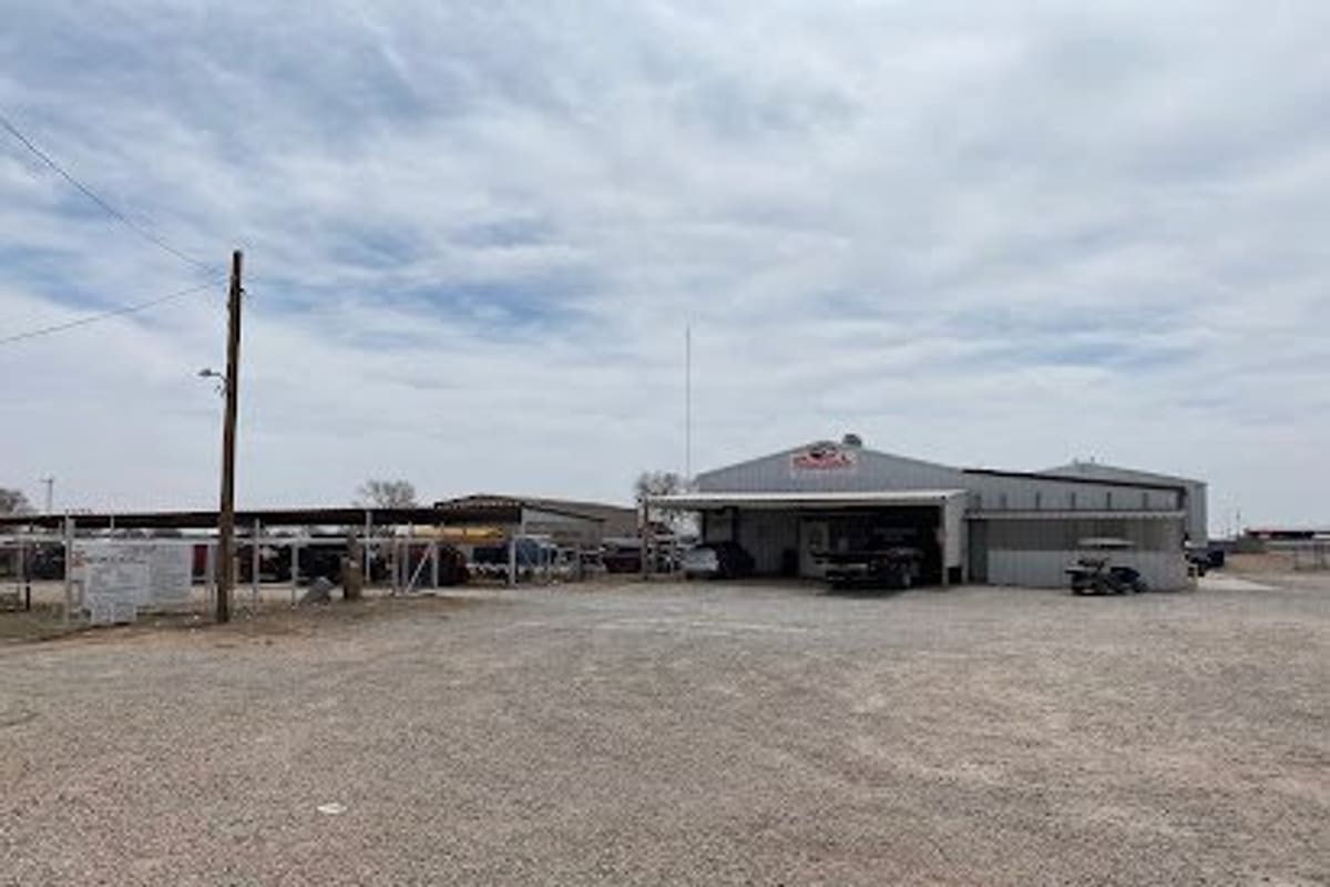 Seminole Auto Salvage: Metal shop building with open bay and covered area beside a wide gravel lot under a cloudy sky