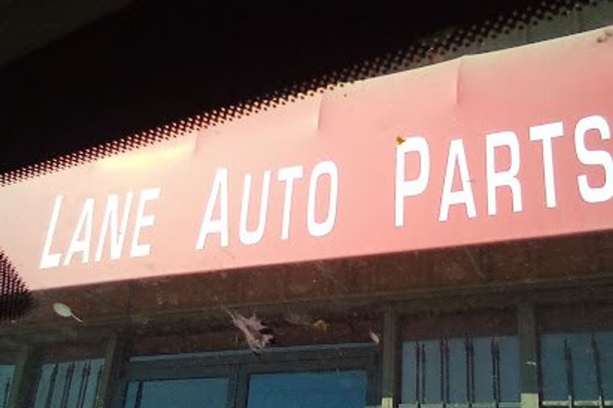 Lane Discount Auto Parts & Salvage: Red storefront sign reading Lane Auto Parts above glass double doors with posted hours Mon-Fri 8-5 and barred windows