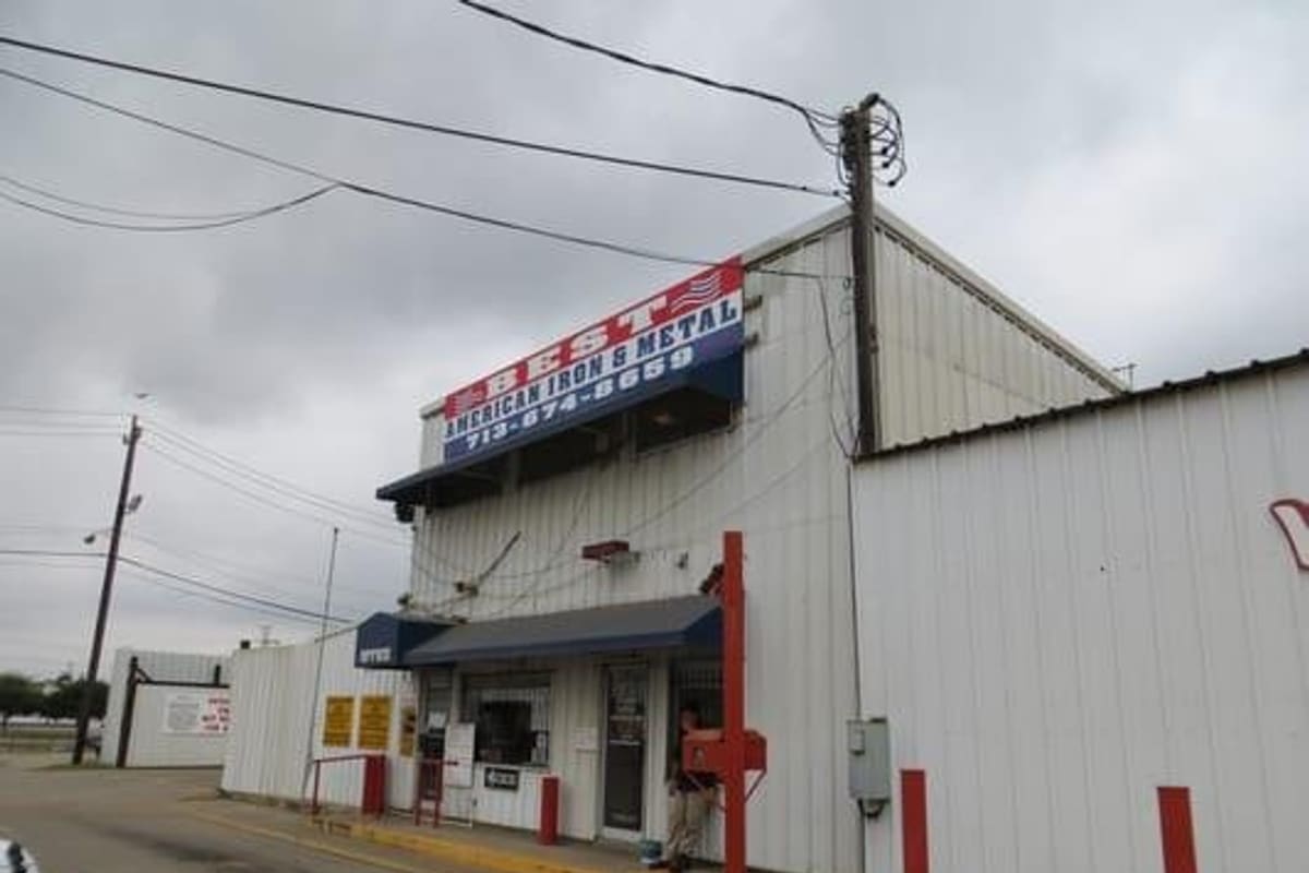 JJ Powell Interests: White metal office building with a red, white and blue sign and a small entrance awning beside a paved lot