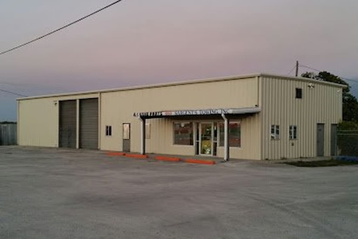 A-1 New & Used Parts: Tan metal commercial building with two garage bay doors, a covered entrance and a large paved lot in front at dusk
