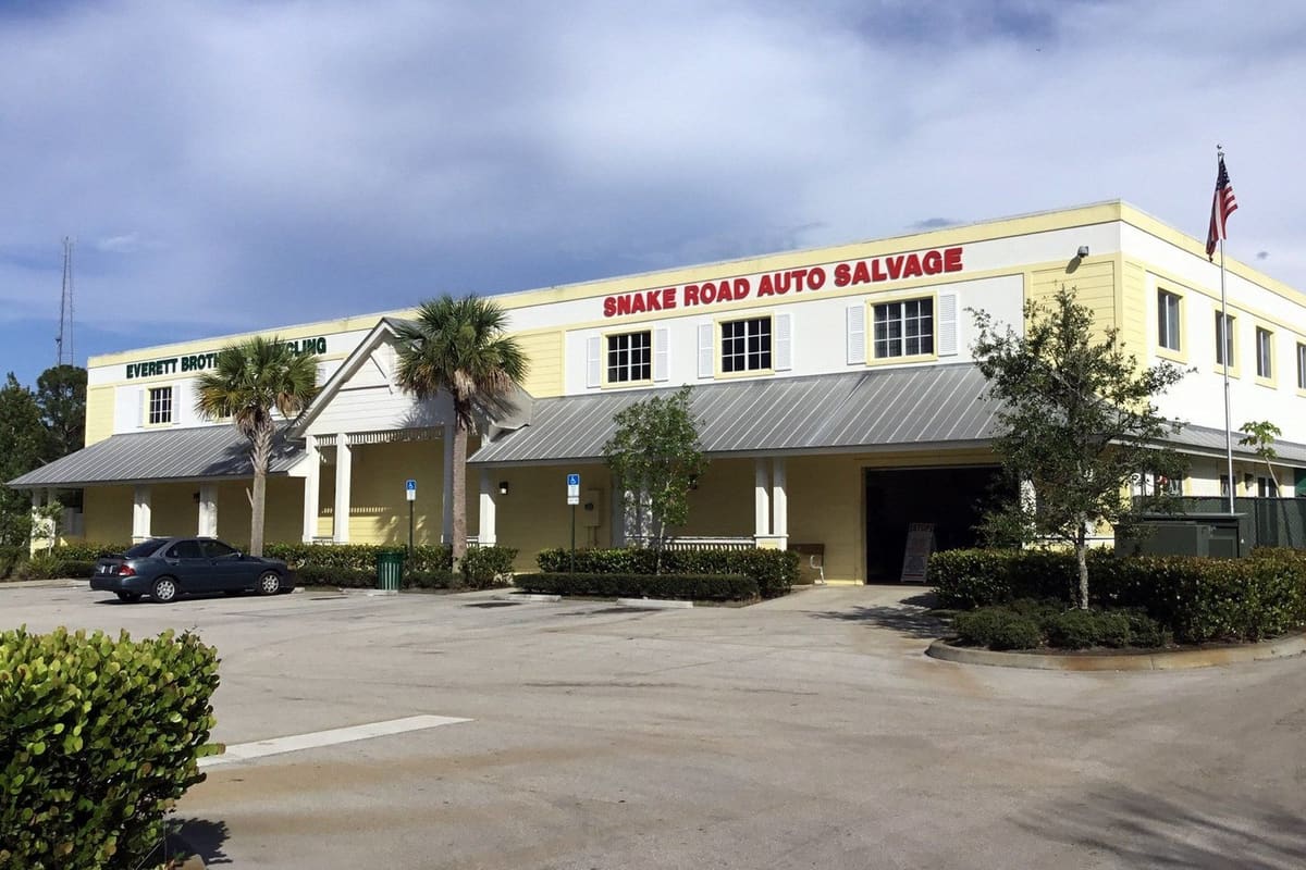 Everett Brothers Recycling: Two-story yellow and white building with a red salvage sign, metal awning, palm trees and a parking lot in front