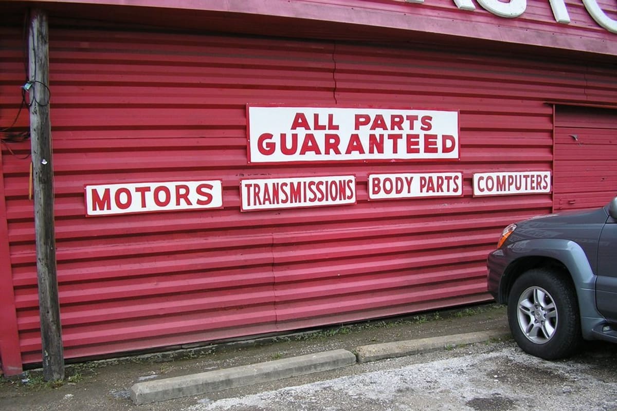 Scott Street Auto Parts: Red corrugated metal building with painted signs for motors, transmissions, body parts and computers, and an SUV parked beside it