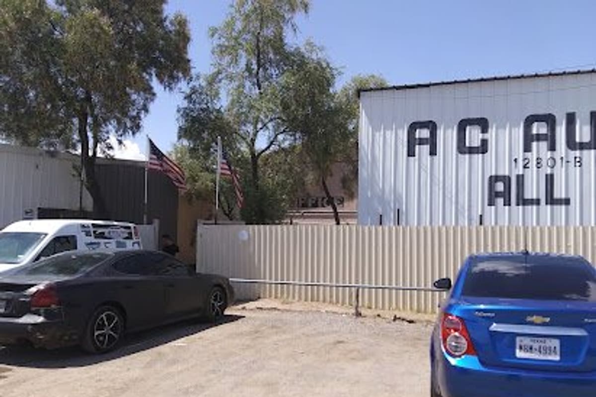 1 Auto Salvage: Gravel entrance to a salvage lot with a corrugated fence, flags, parked cars and a white metal building with partial lettering