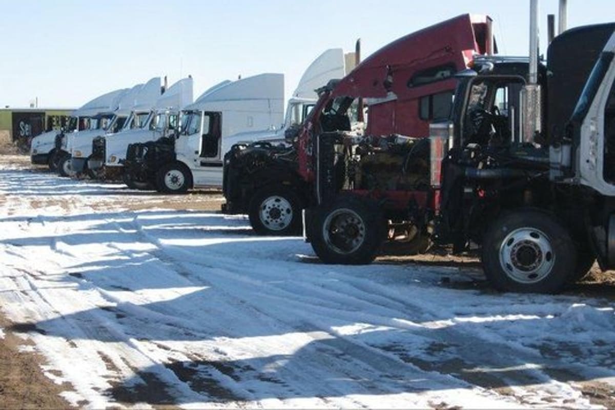 Active Truck & Auto Parts: Row of semi truck cabs with hoods open parked on a snowy dirt lot under a clear sky