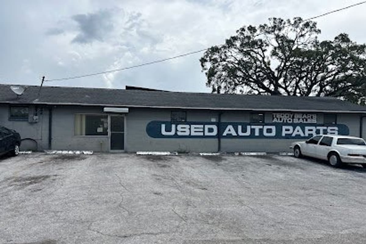 Teddy Bears Auto Parts & Salvage: Single-story gray building with a large painted Used Auto Parts sign and a cracked parking lot in front