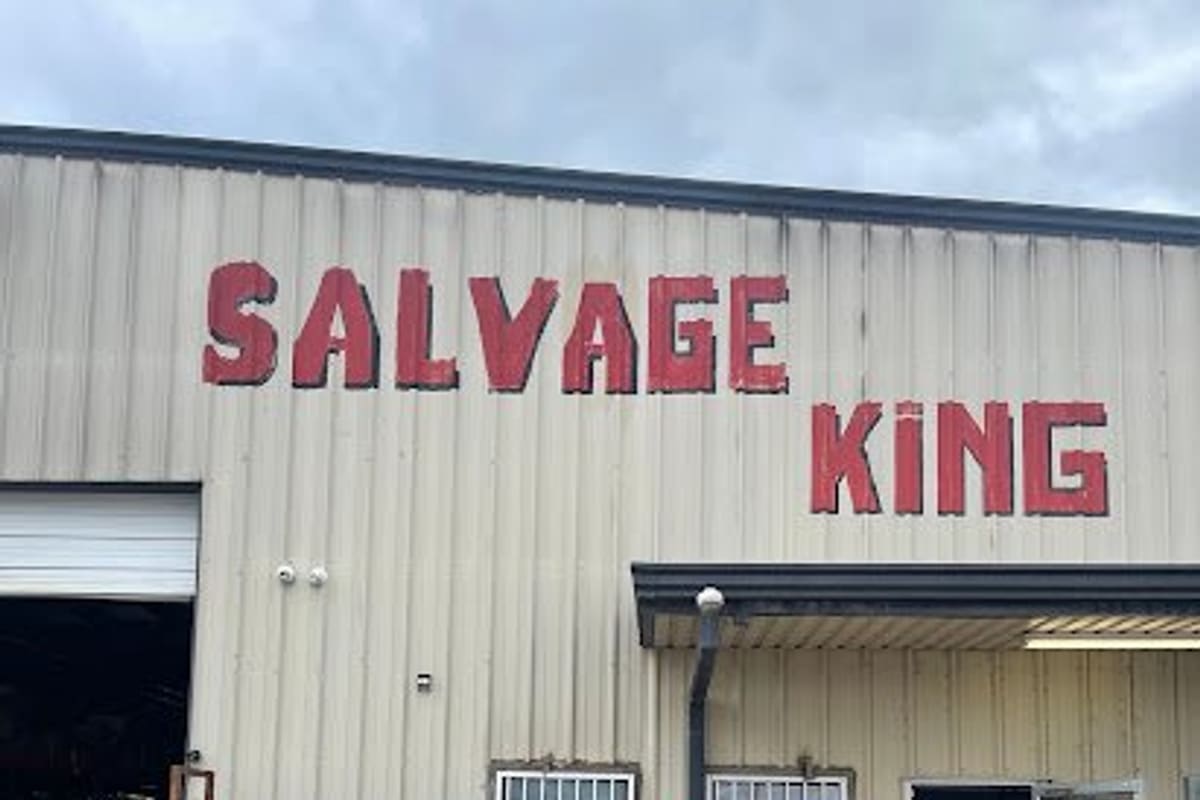 Salvage King: Metal warehouse building with large red lettering, stacked used tires, a ladder and an open barred door on a concrete lot