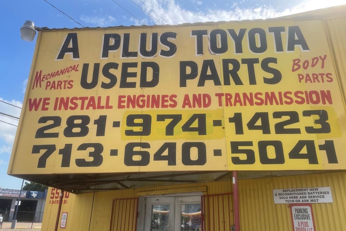 A+ Toyota Used Parts: Large yellow sign above a metal storefront advertising used Toyota parts, engine and transmission installs, and phone numbers