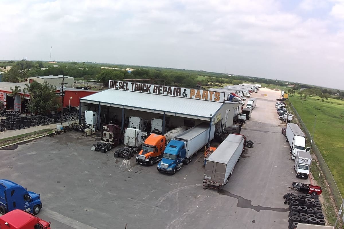 CC Truckers: Aerial view of a truck repair shop with a large sign, semi trucks parked in front, and a wide paved lot