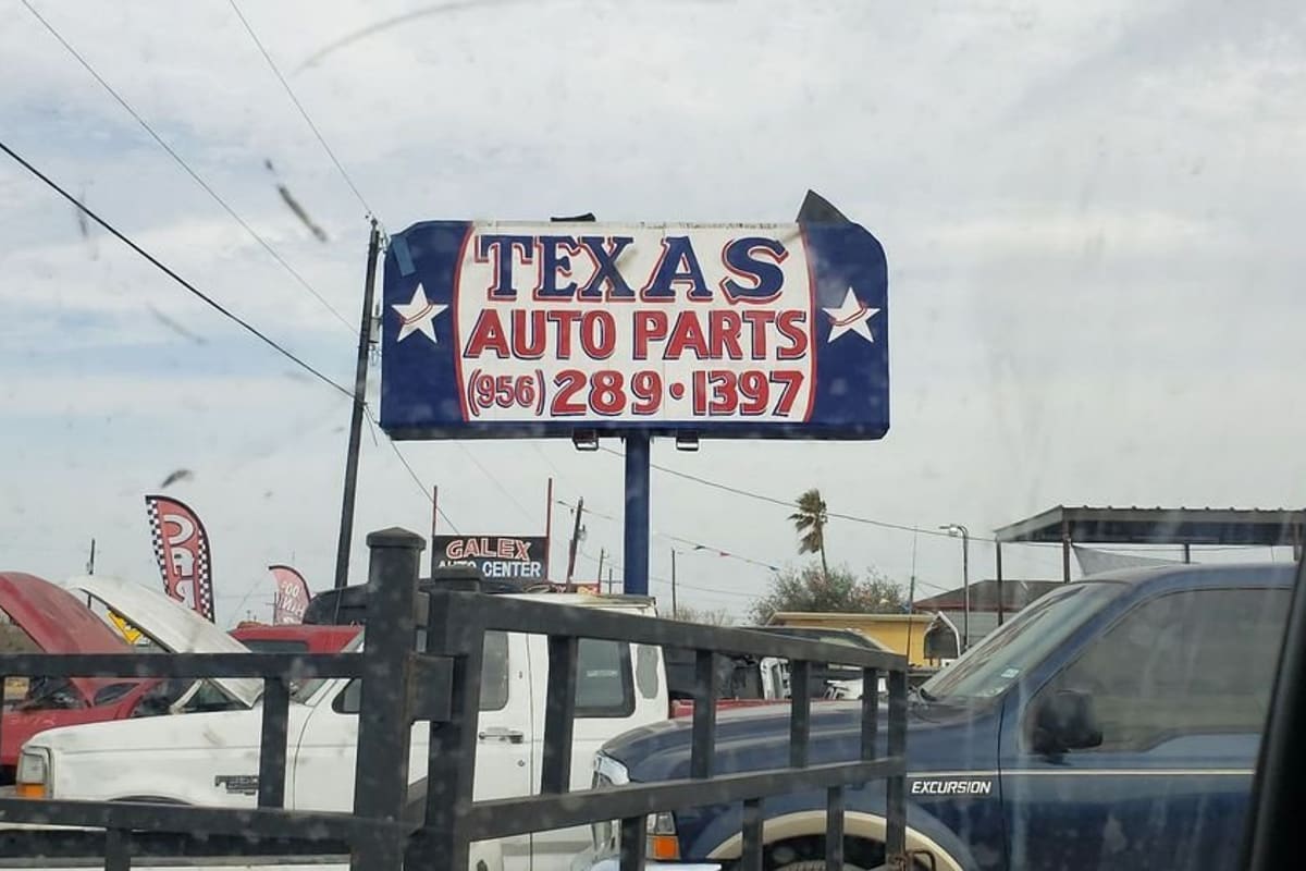 Texas Auto Parts: Large blue and white roadside sign reading Texas Auto Parts above a yard of trucks and cars behind a fence