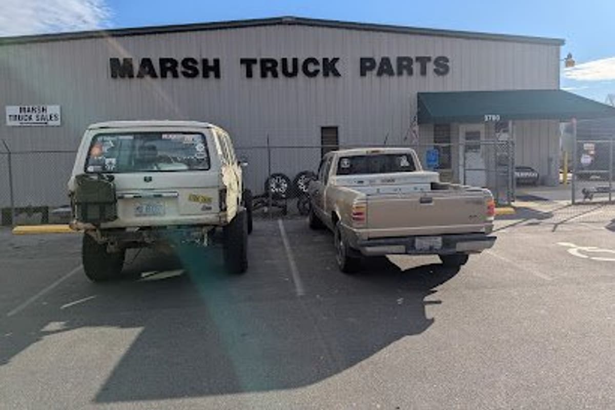 Marsh Auto Parts Truck Division: Metal warehouse building with large black Truck Parts lettering, a green awning entrance and two pickups parked in front