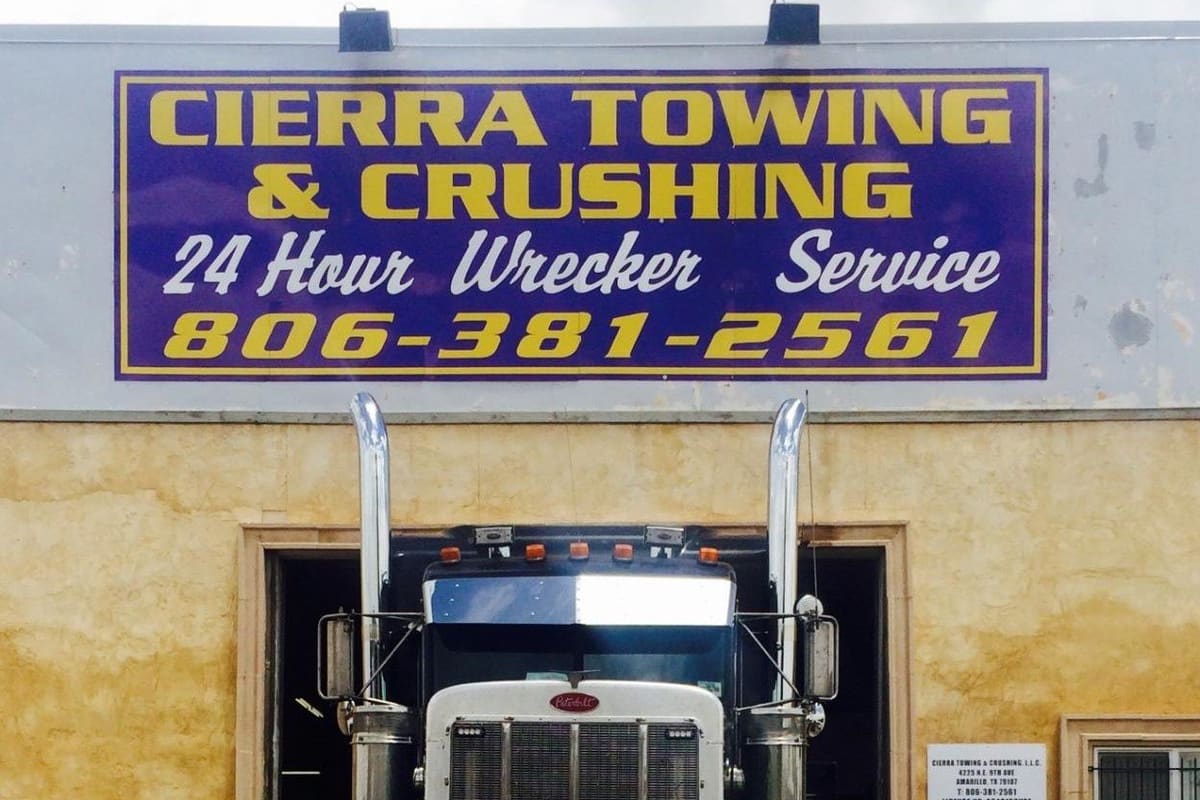 Cierra Towing and Crushing: Large tow truck parked in front of a tan stucco building with a big blue and yellow towing service sign above