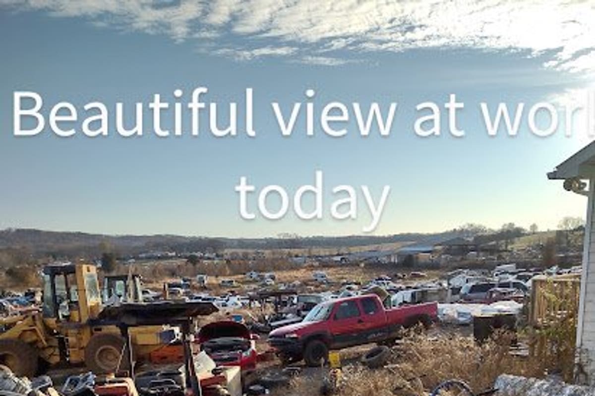 Purdy's Auto Parts & Salvage: Wide daytime view of a salvage yard with a backhoe, a red pickup and many vehicles spread across open land