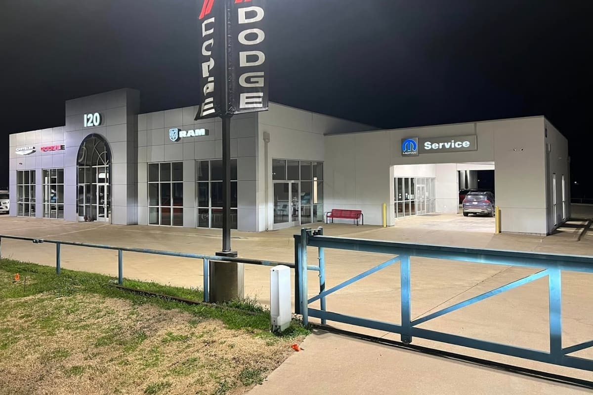 Jeep Junkies of Texas: Night view of a gray dealership-style building with a tall banner pole, a service bay and a blue metal gate in front