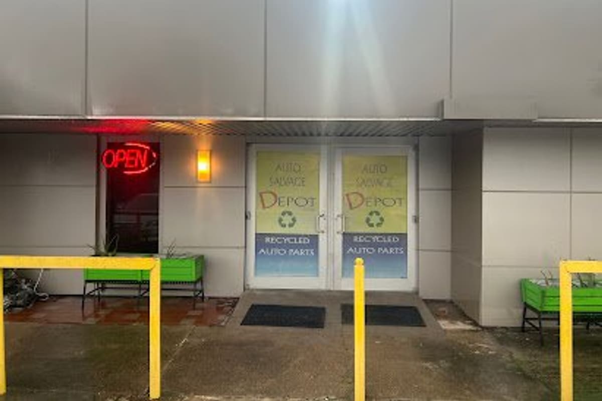 Auto Salvage Depot: Glass double doors with recycled auto parts window graphics, a red open sign, and yellow bollards out front