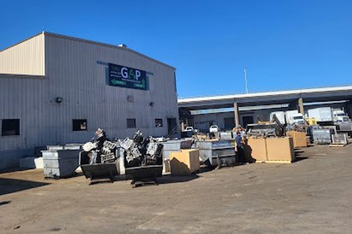 Gold Auto Parts Recycling: Large metal warehouse building beside an open dirt lot filled with bins of scrap engine parts under a clear blue sky