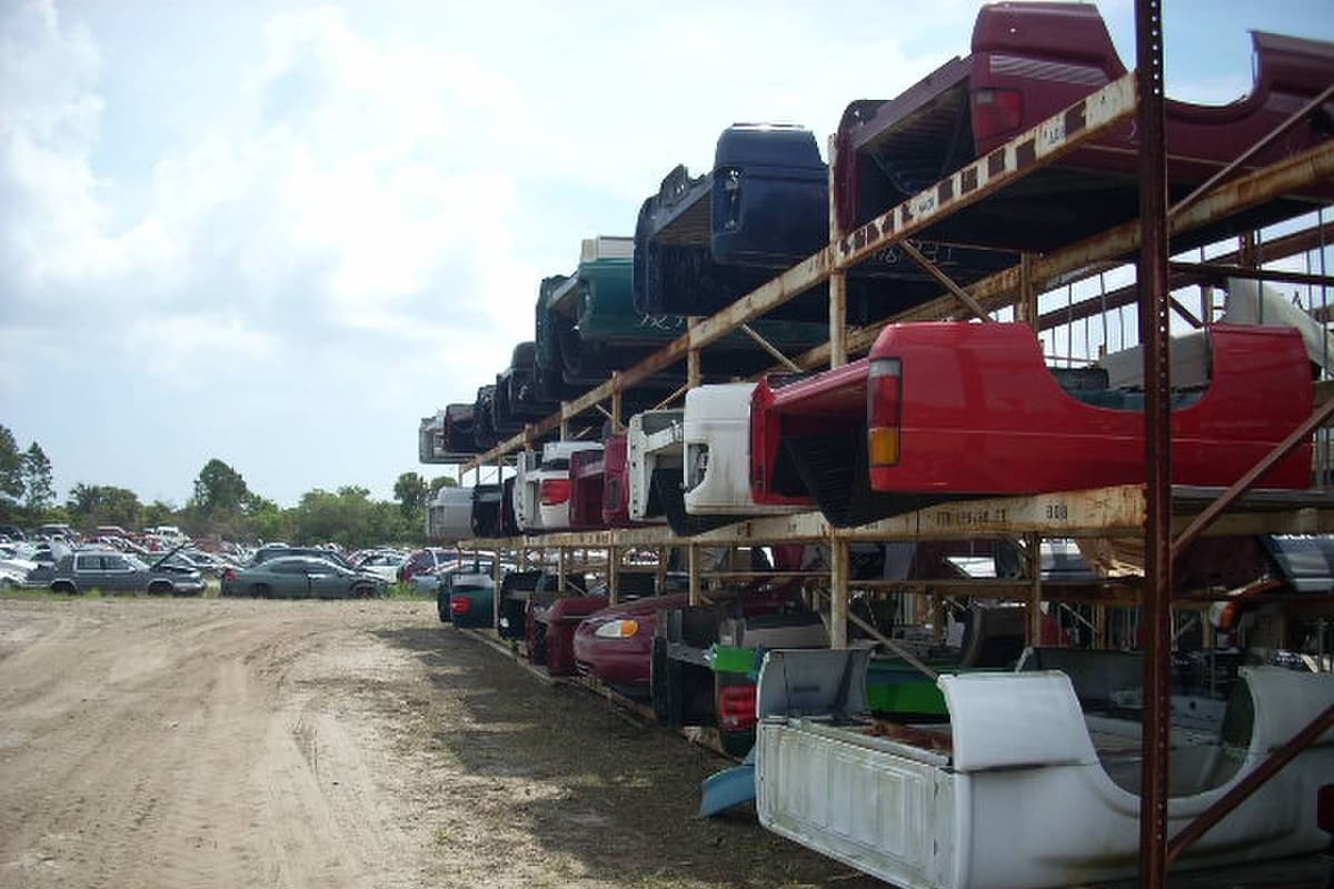 E. Quarno & Sons Auto Salvage: Dirt lane in a salvage yard beside tall racks of truck beds, with rows of vehicles in the distance
