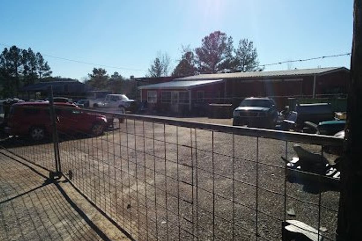 Lambert's Used Cars & Parts: Gravel lot behind a wire fence with parked cars and trucks in front of a red building on a sunny day