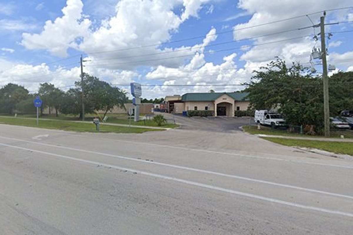 LKQ Fort Myers: Street view of a tan single-story building with a green roof, driveway entrance, pole sign, and parked vehicles