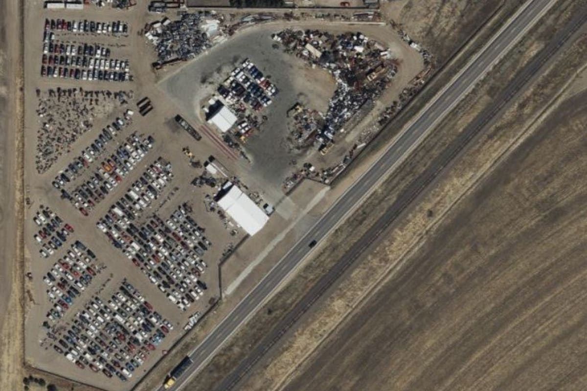 Andersen's U-Pull-It: Aerial view of a self-service salvage yard with rows of parked vehicles beside a highway and farm fields
