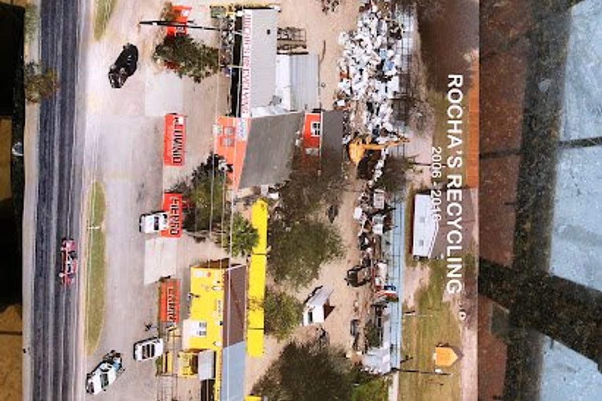 Scrap Metal Recycling: Aerial view of a scrap yard with buildings, orange signs, trees and piles of scrap metal beside a road